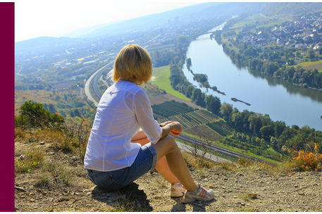 Sitzende Frau blickt von einer Klippe auf einen Fluß, Rücken zur Kamera