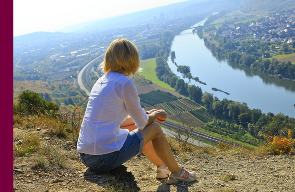 Sitzende Frau blickt von einer Klippe auf einen Fluß, Rücken zur Kamera (Wird bei Klick vergrößert)