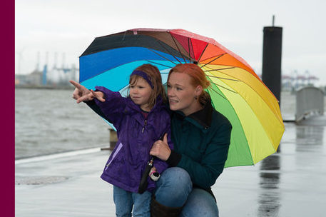 Mutter und kleine Tochter unter einem regenbogenfarbenen Schirm