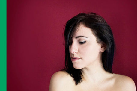 Porträt einer jungen Frau mit nackten Schultern vor dunkelrotem Hintergrund