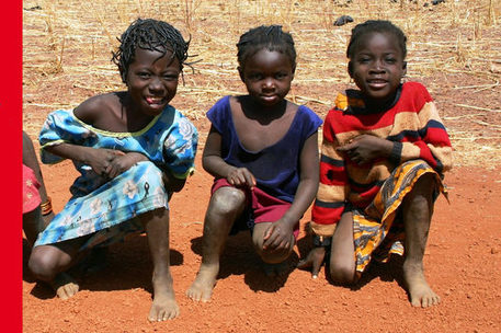 Drei afrikanische Mädchen , die auf einer roten Erde hocken