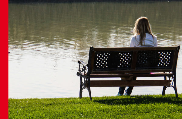 Eine Frau sitzt an einem See auf der Bank.