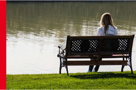 Frau von hinten auf einer Bank sitzend am See