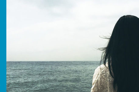 Schwarzhaarige Frau blickt auf das Meer, kein Land sichtbar