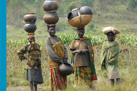 Vier afrikanische Frauen und Mädchen auf dem Feld mit Lasten auf den Köpfen