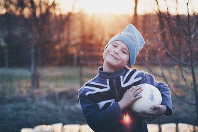 Ein Kind lächelt in die Kamera und hält einen Ball unter dem Arm