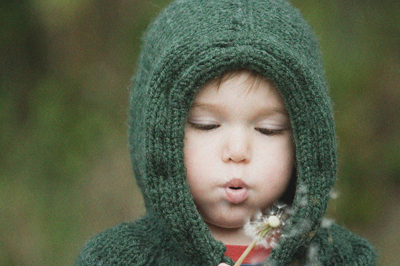 Ein Kind mit Kapuze pustet auf eine Pusteblume