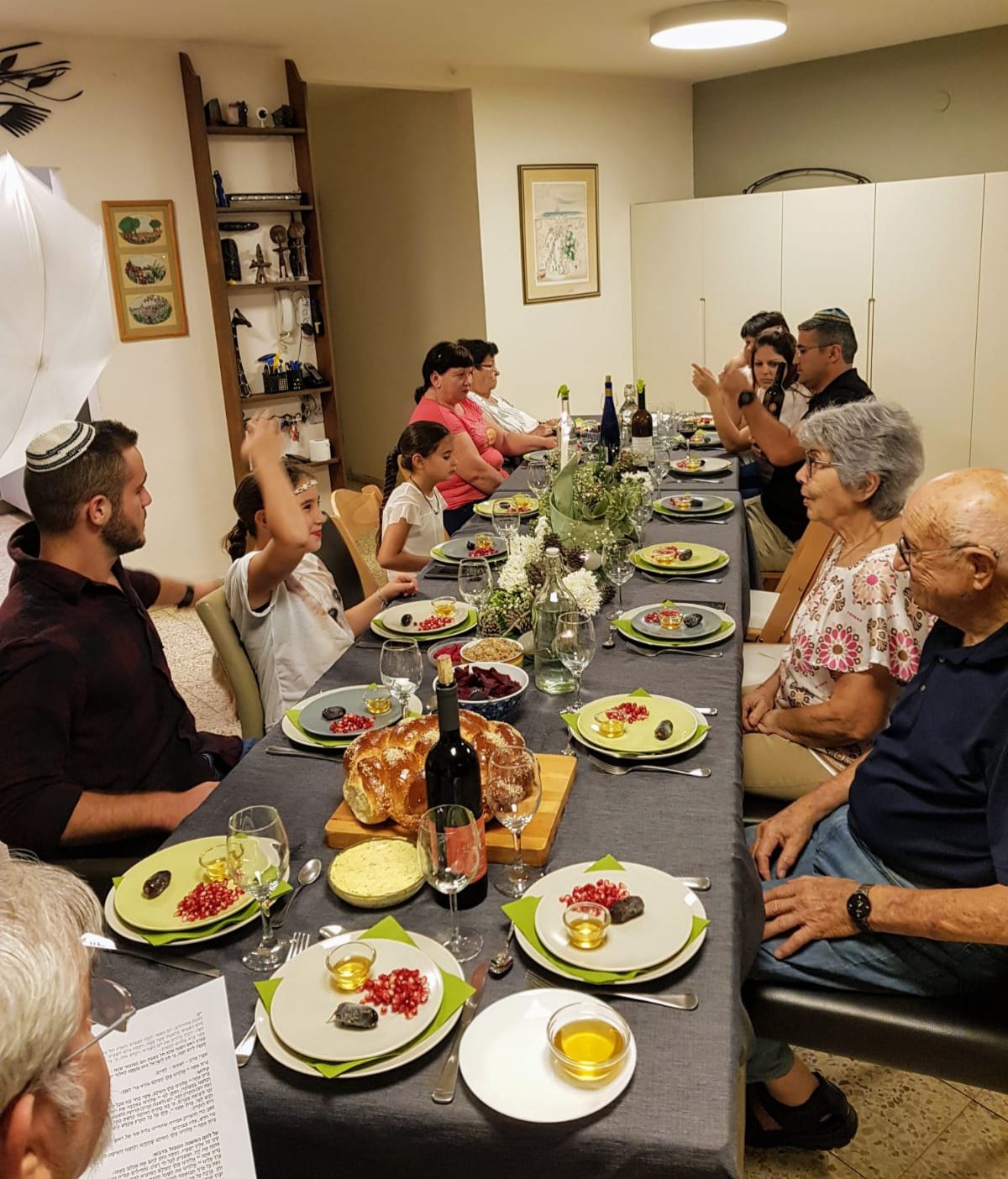 Das Foto zeigt Familie und Freunde beim Neujahrsmahl mit Granatäpfelkernen, Honig, Datteln und dem süßen Hefezopf Challa..