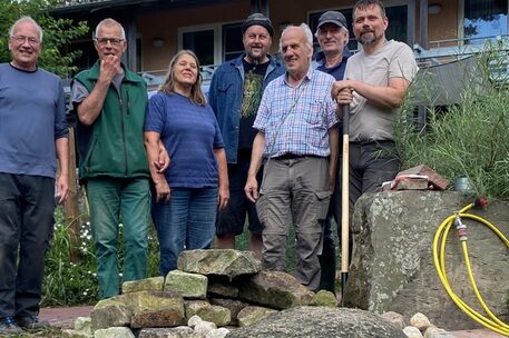 Eine Personengruppe steht mit Werkzeug im Garten.