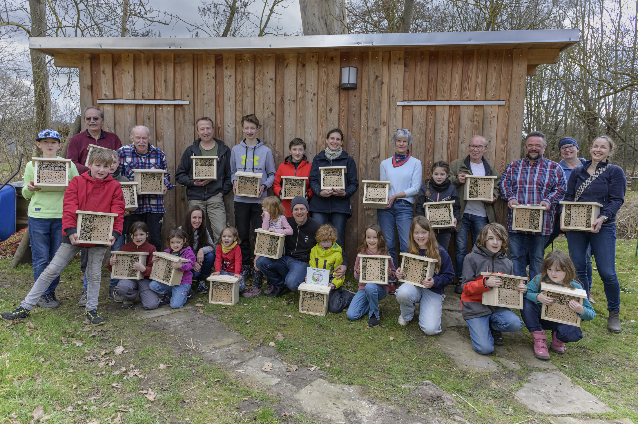 Eine Gruppe Kinder und Erwachsene stehen vor einem Schuppen und halten selbstgebaute Insektenhotels in den Händen. (Wird bei Klick vergrößert)