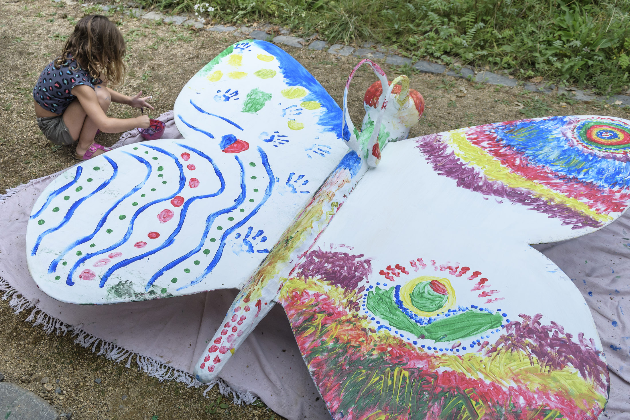 Kinder bemalen einen großen Schmetterling aus Pappe mit bunten Farben. (Wird bei Klick vergrößert)