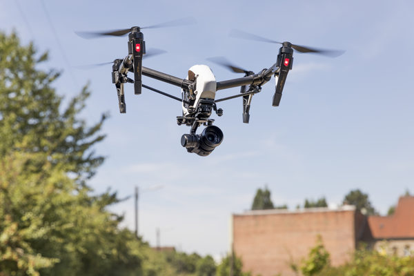Eine Drohne fliegt vor Grünflächen und Häusern.