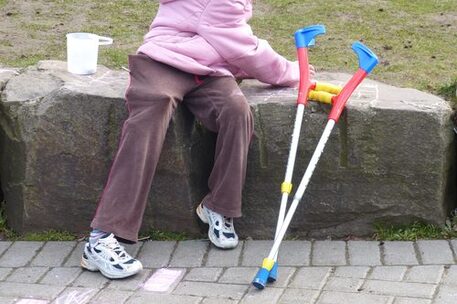 Kind mit Krücken auf einem Stein sitzend