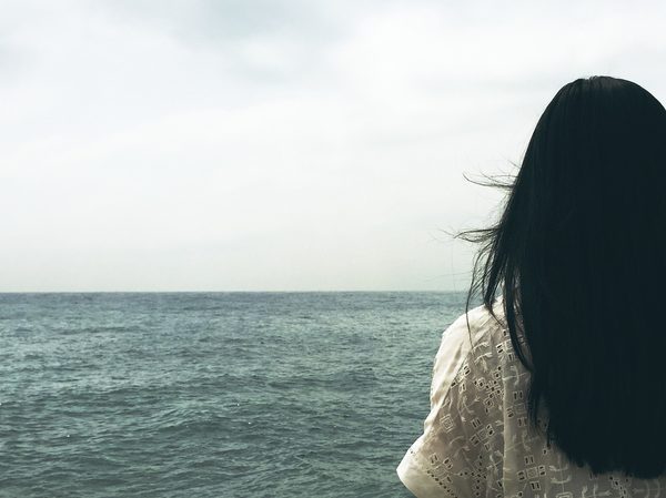Rücken einer dunkelhaarigen Frau, die auf das Meer blicktz (Wird bei Klick vergrößert)