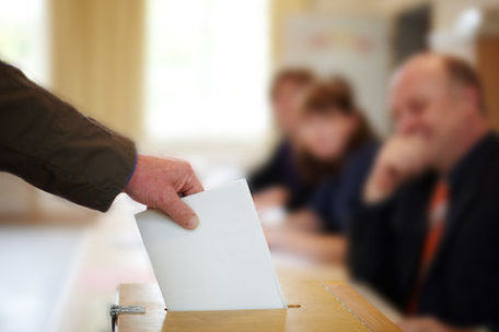 Das Bild zeigt, wie ein Stimmzettel in eine Wahlurne gesteckt wird.