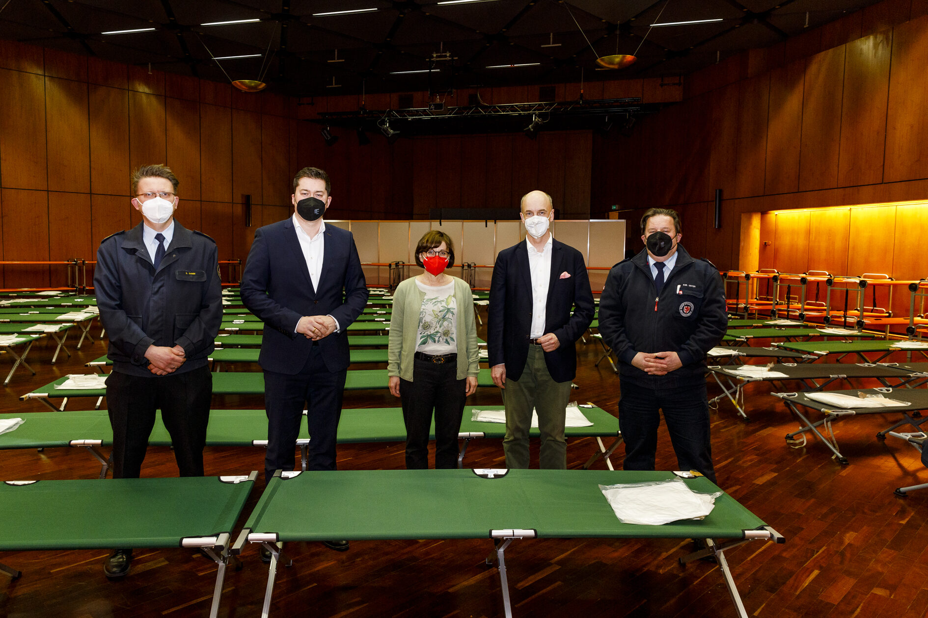 Fünf Personen stehen zwischen den Behelfsbetten in der Stadthalle. (Wird bei Klick vergrößert)