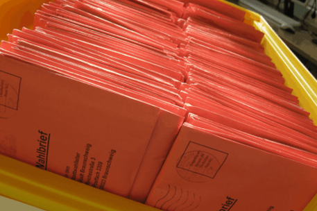 Gelbe Transportkiste mit roten Wahlbriefen als Symbol für die Briefwahl