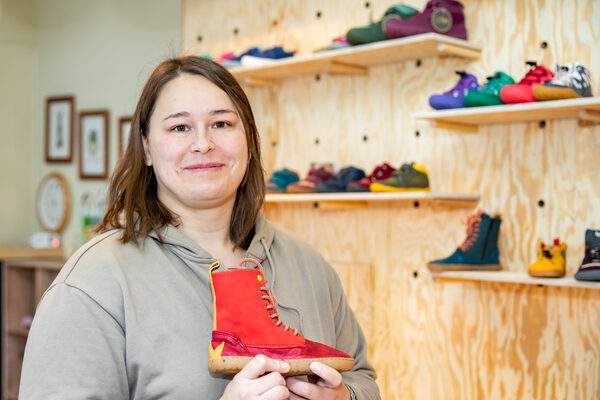 Das Bild zeigt die Inhaberin des Ladens "Wald Child" mit einem roten Barfußschuh in den Händen. (Wird bei Klick vergrößert)