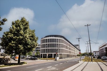 Das Bild zeigt das Kontorhaus in Braunschweig in der Mitte. Rechts sind Straßenbahnschienen und links ist ein Baum zu sehen.
