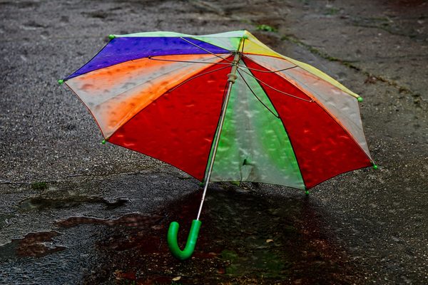 Das Bild zeigt einen bunten Regenschirm, der auf dem nassen Asphalt einer Straße liegt.