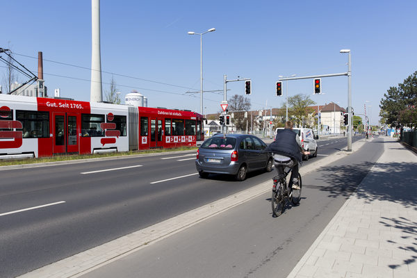 Das Bild zeigt zwei Autos auf einer Straße in Braunschweig, die vor einer Ampel stehen. Ebenso sind eine Straßenbahn und ein Radfahrer zu sehen.