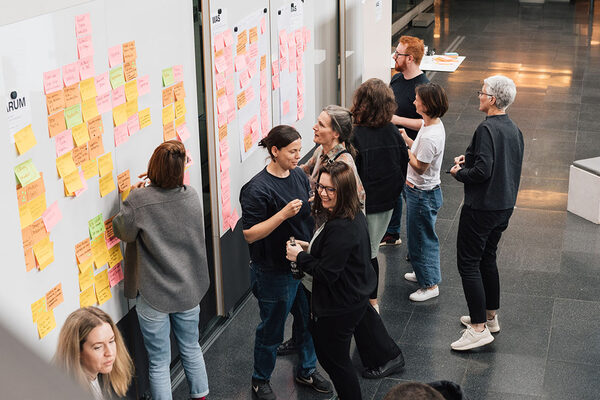 Menschen vor Whiteboard mit bunten Zetteln (Wird bei Klick vergrößert)
