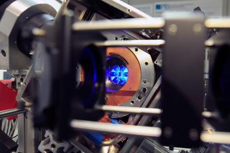 Nahaufnahmen des aktuellen Vakkumsystems, in dem man die blaue Fluoreszenz einer Wolke lasergekühlter Strontium-Atome und ihre Reflektion in Spiegeln sieht, die für die Laserkühlung wichtig sind.