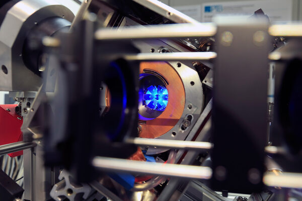 Nahaufnahmen des aktuellen Vakkumsystems, in dem man die blaue Fluoreszenz einer Wolke lasergekühlter Strontium-Atome und ihre Reflektion in Spiegeln sieht, die für die Laserkühlung wichtig sind. (Wird bei Klick vergrößert)