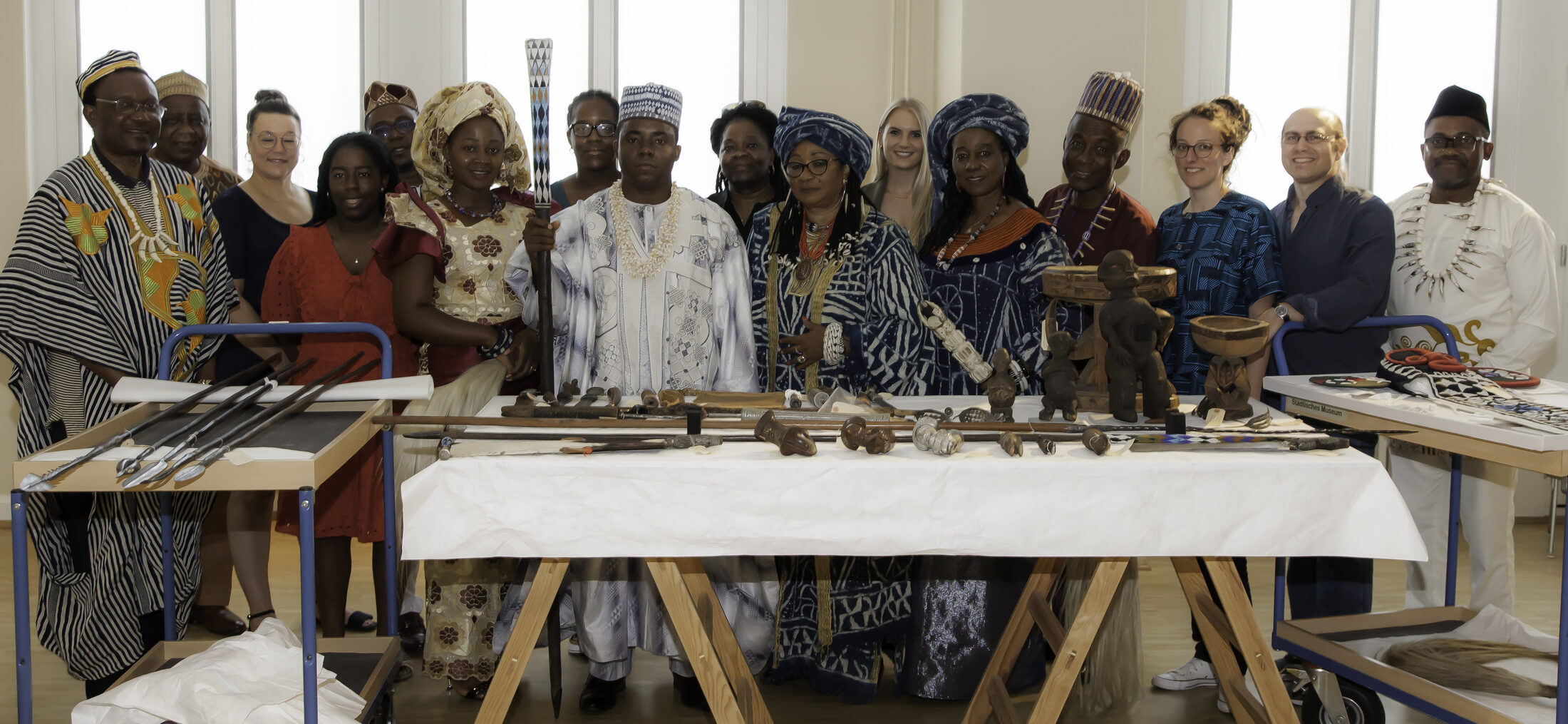 Foto der Bangwa-Delegation, Museumsmitarbeiterinnen und Mitarbeitern vor Objekten aus dem Bangwa Königreich «Lebang» (Wird bei Klick vergrößert)