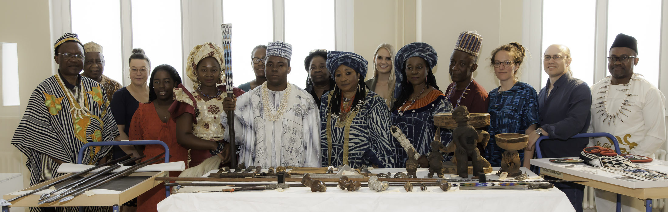 Foto der Bangwa-Delegation, Museumsmitarbeiterinnen und Mitarbeitern vor Objekten aus dem Bangwa Königreich «Lebang» (Wird bei Klick vergrößert)