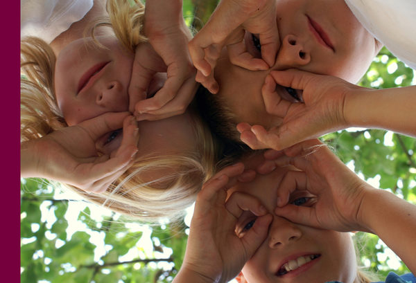 Drei Kinder blicken durch ihre Finger in die Kamera