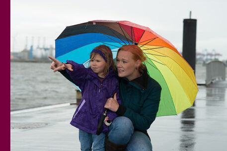 Mutter und kleine Tochter unter einem regenbogenfarbenen Schirm