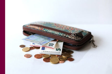 Bunte Geldbörse, aus der ein paar Geldscheine ragen, davor Münzen