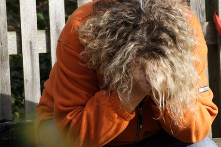 Frau auf einer Parkbank, Gesicht in den Händen