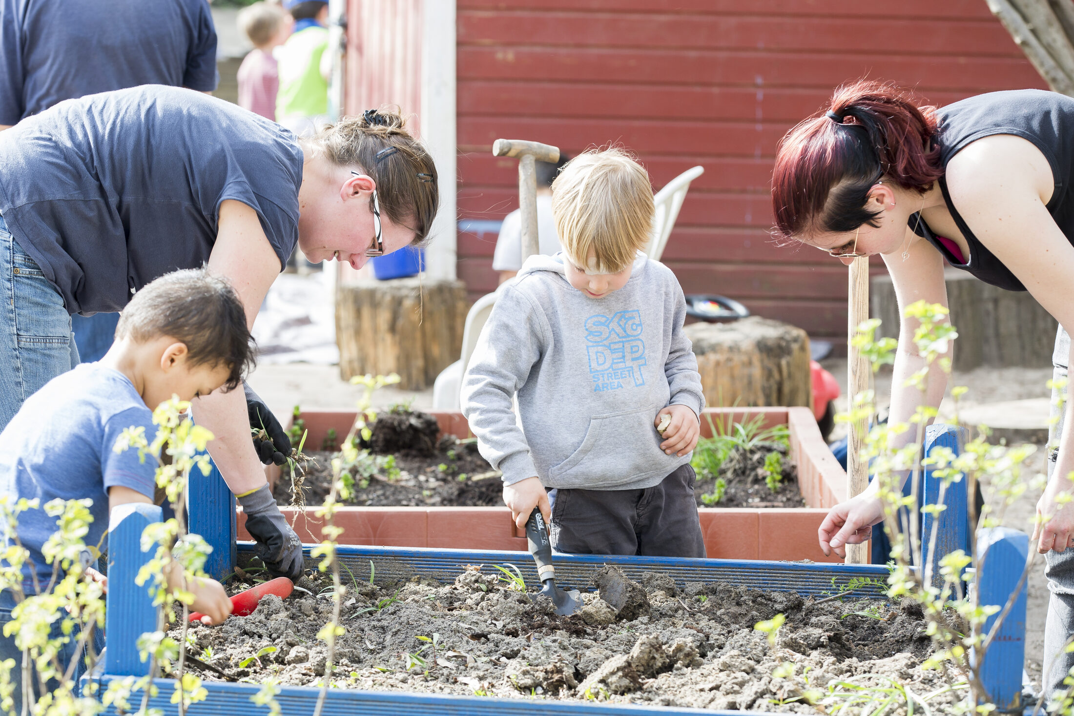 Hier gärtnern zwei Frauen mit zwei Kindern in einem Hochbeet (Wird bei Klick vergrößert)