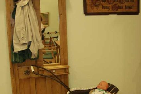 Garderobe mit Spiegel, Jacke, Hut, Bild an der Wand, davor alter Puppenwagen