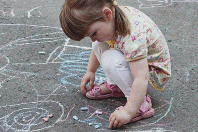 Ein Kind hockt auf dem Boden und malt mit Kreide