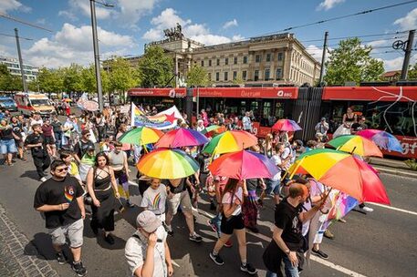 Eine Menschengruppe mit bunten Regenschirmen ausgestattet im CSD Demonstrationszug vor dem Schloss