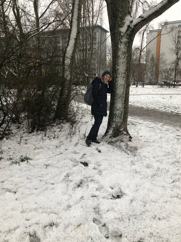 Eine Person steht im Schnee neben einem Baum und lächelt