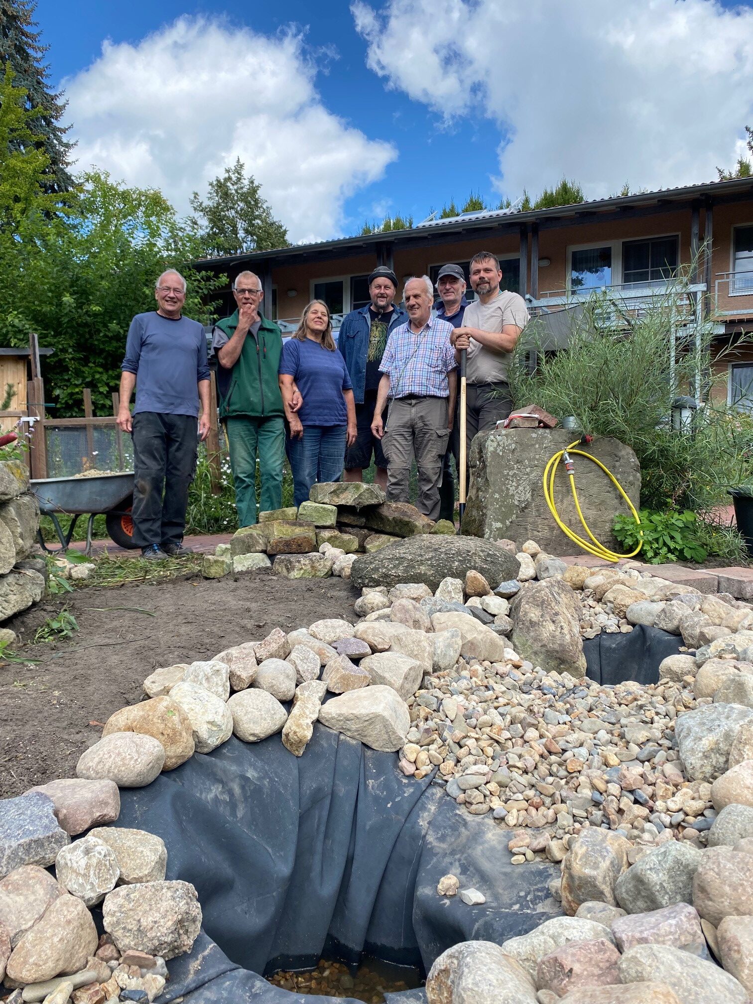 Eine Gruppe Personen steht legt einen Gartenteich an. (Wird bei Klick vergrößert)