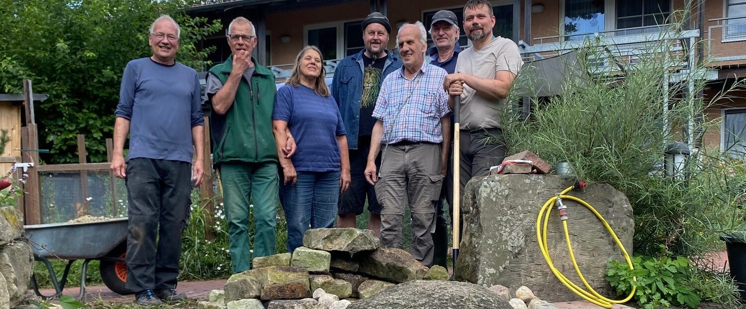 Eine Personengruppe steht mit Werkzeug im Garten.