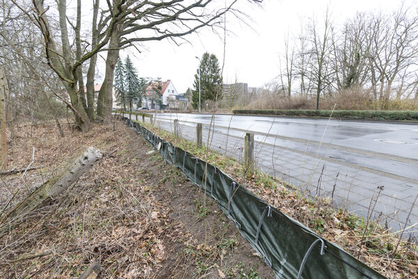 Am Rand einer Straße ist ein Zaun mit einer Folie befestigt.