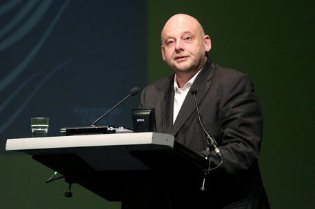2014 gewann Thomas Hettche den Wilhelm Raabe-Literaturpreis. Ein Foto zeigt den Preisträger. Er steht am Rednerpult, hat eine Glatze und schaut in Richtung des Publikums. Außerdem trägt er ein schwarzes Jackett