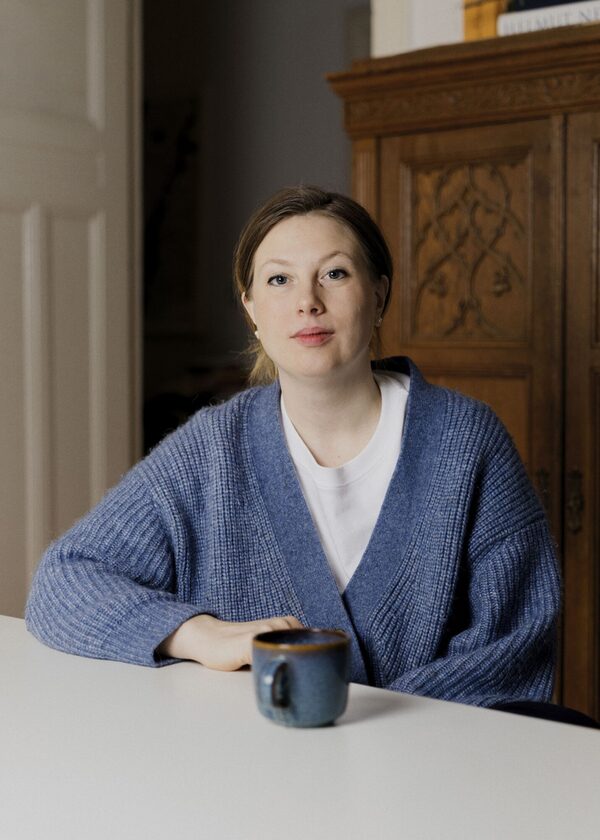 Autorin Hannah Lühmann, Ende 30, sitzt am Tisch mit einer Kaffeetasse und schaut frontal in die Kamera. (Wird bei Klick vergrößert)