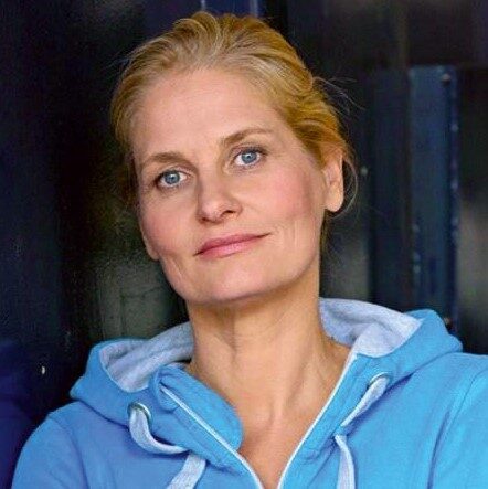 Kathrin Reinhardt sieht in die Kamera, hat einen blauen Zipper-Pullover an, zurückgebundenes blondes Haar und blaue Augen (Wird bei Klick vergrößert)