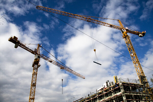 Zwei Baukräne vor blauem Himmel mit einem Neubau (Wird bei Klick vergrößert)