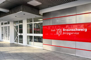 Gebäudeeingang mit weißer Tür und einem roten Schild mit Schrift Stadt Braunschweig Bürgerservice