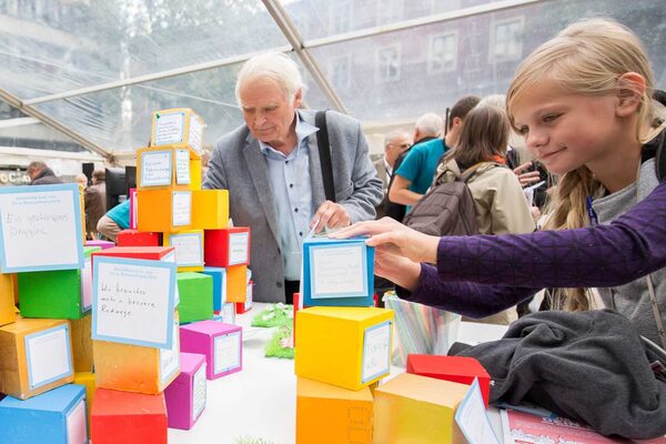 Ein älterer Herr und ein Mädchen heften ihre Ideen für die Stadtentwicklung an Stapel aus bunten Bauklötzen (Wird bei Klick vergrößert)