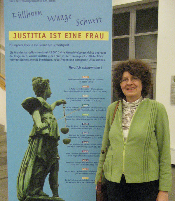Frau vor Ausstellungsplakat mit dem Titel: Justitia ist eine Frau" (Wird bei Klick vergrößert)