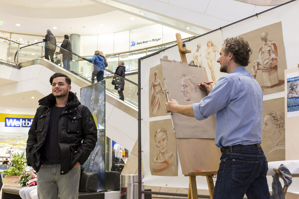 Die winterkunstzeit verwandelt am 9. und 10. Februar viele Orte der Innenstadt in Ateliers. 2017 portraitierte Magnus Kleine-Tebbe (rechts) Gäste in den Schloss-Arkaden, dieses Jahr zeichnet er in der Buchhandlung Graff. (Wird bei Klick vergrößert)